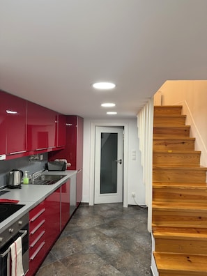 A modern kitchen with red cabinets, a stainless steel sink, and a wooden staircase. - Romantic Alfama - Duplex Apartment in Lisbon, Alfama (Lisboa)