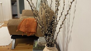 A living room with a wooden coffee table, a vase with branches, a sofa with a throw blanket, and a door leading to another room. - Romantic Alfama - Duplex Apartment in Lisbon, Alfama (Lisboa)