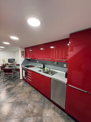 A modern kitchen with red cabinets, stainless steel appliances, and a tiled floor.