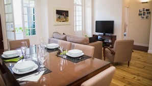 A dining area with a wooden table set for four, a sofa, and a television in the background.