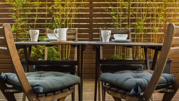 A wooden deck with two tables and chairs, bamboo plants in the background, and a wooden fence.