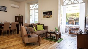 A living room with a wooden floor, a sofa, a coffee table, a dining area with chairs, and a TV.