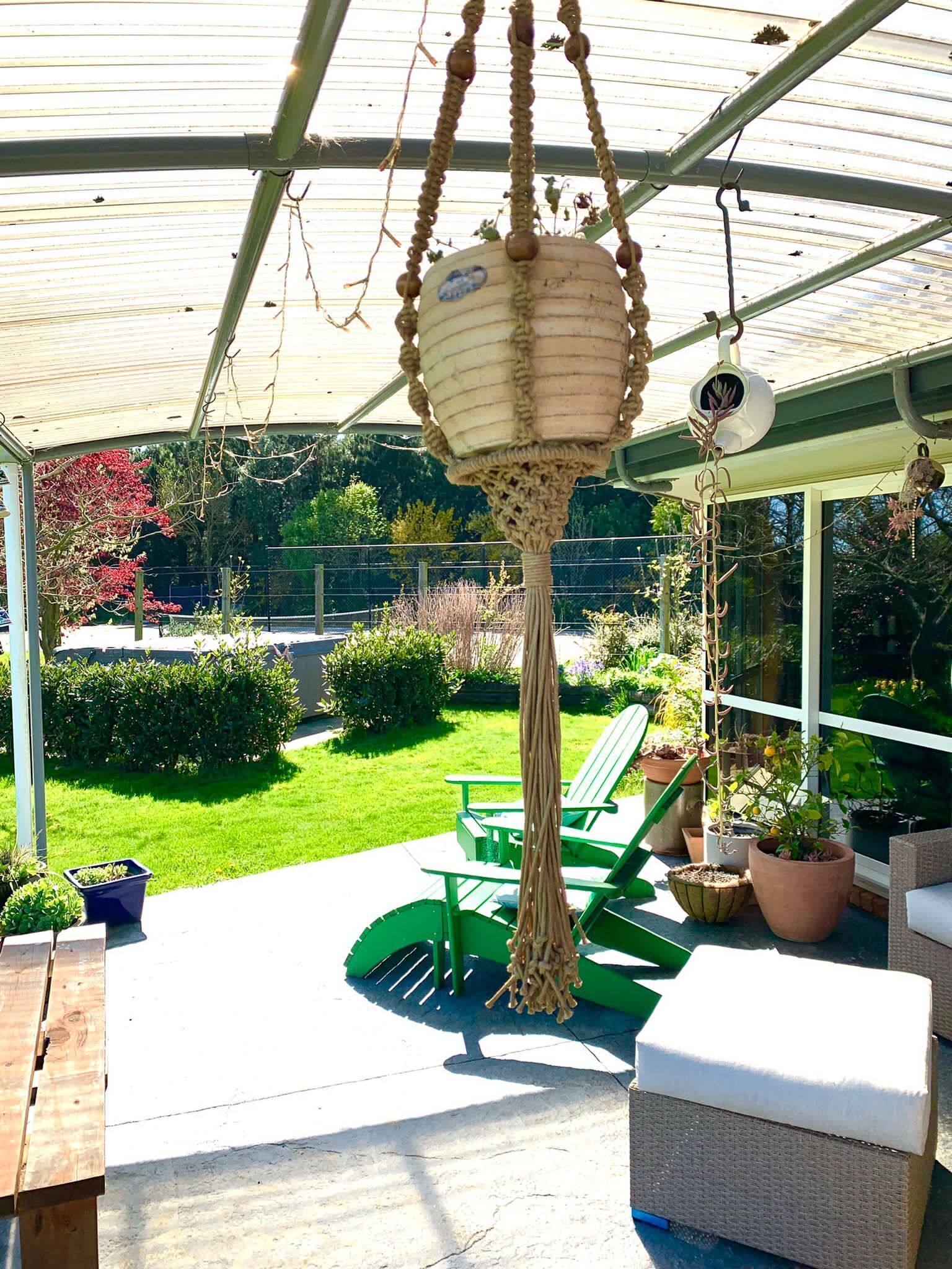 A covered patio area with a hanging planter, green chairs, and potted plants.