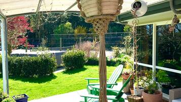 A covered patio area with a hanging planter, green chairs, and potted plants.