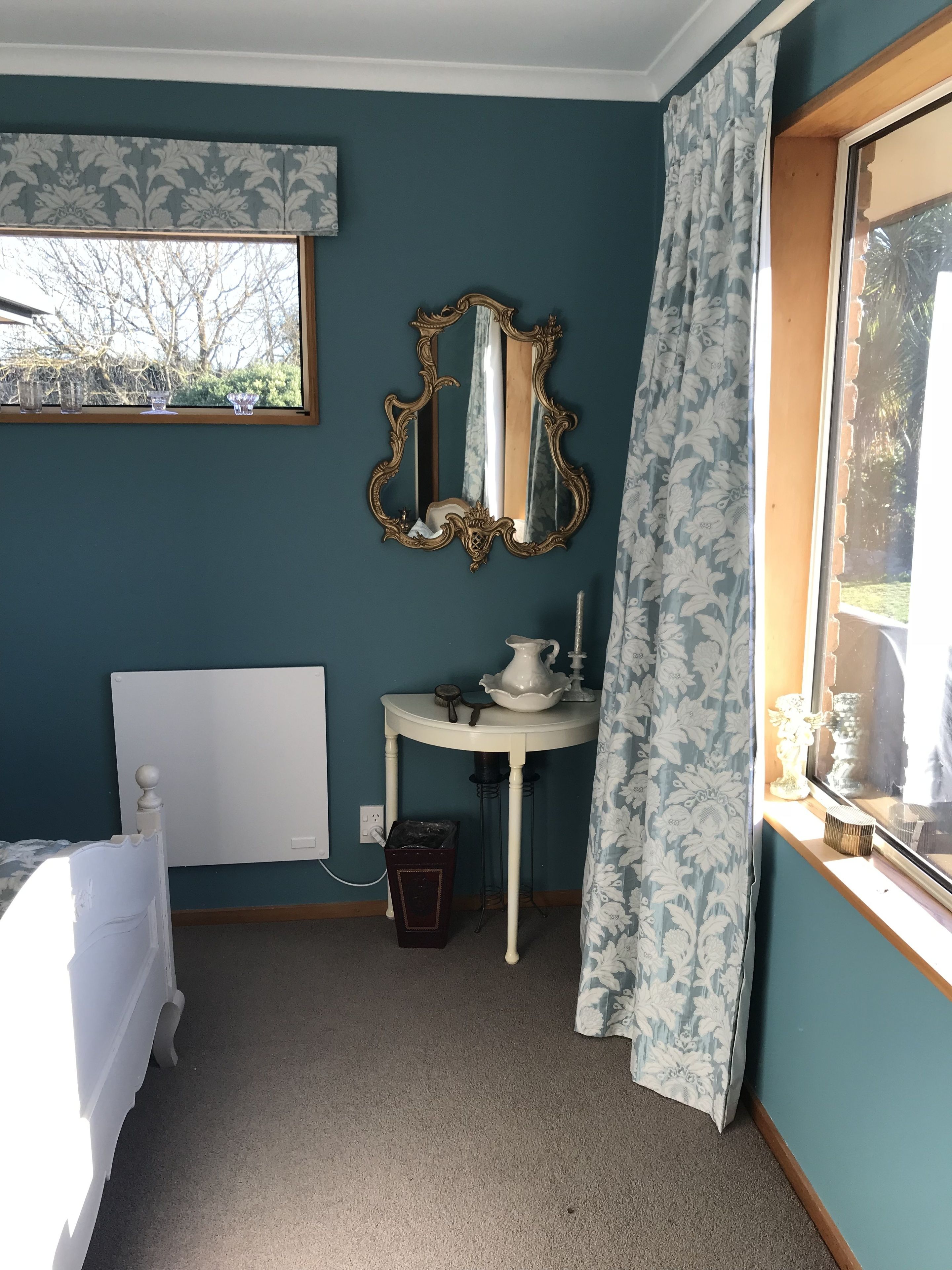 Une chambre à coucher avec un lit, une table de chevet avec une lampe, un miroir et une fenêtre avec des rideaux.