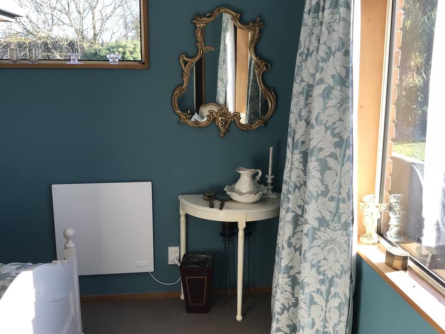 Une chambre à coucher avec un lit, une table de chevet avec une lampe, un miroir et une fenêtre avec des rideaux.