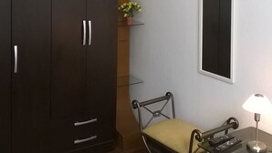 A room with a large wardrobe, a small table with a lamp, a chair, and a mirror on the wall. - Casa Bella Lima (Lima)