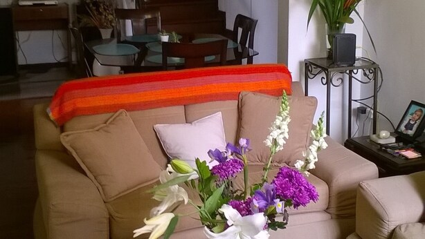 A living room with a beige sofa, a coffee table with a vase of flowers, and a staircase in the background. - Casa Bella Lima (Lima)