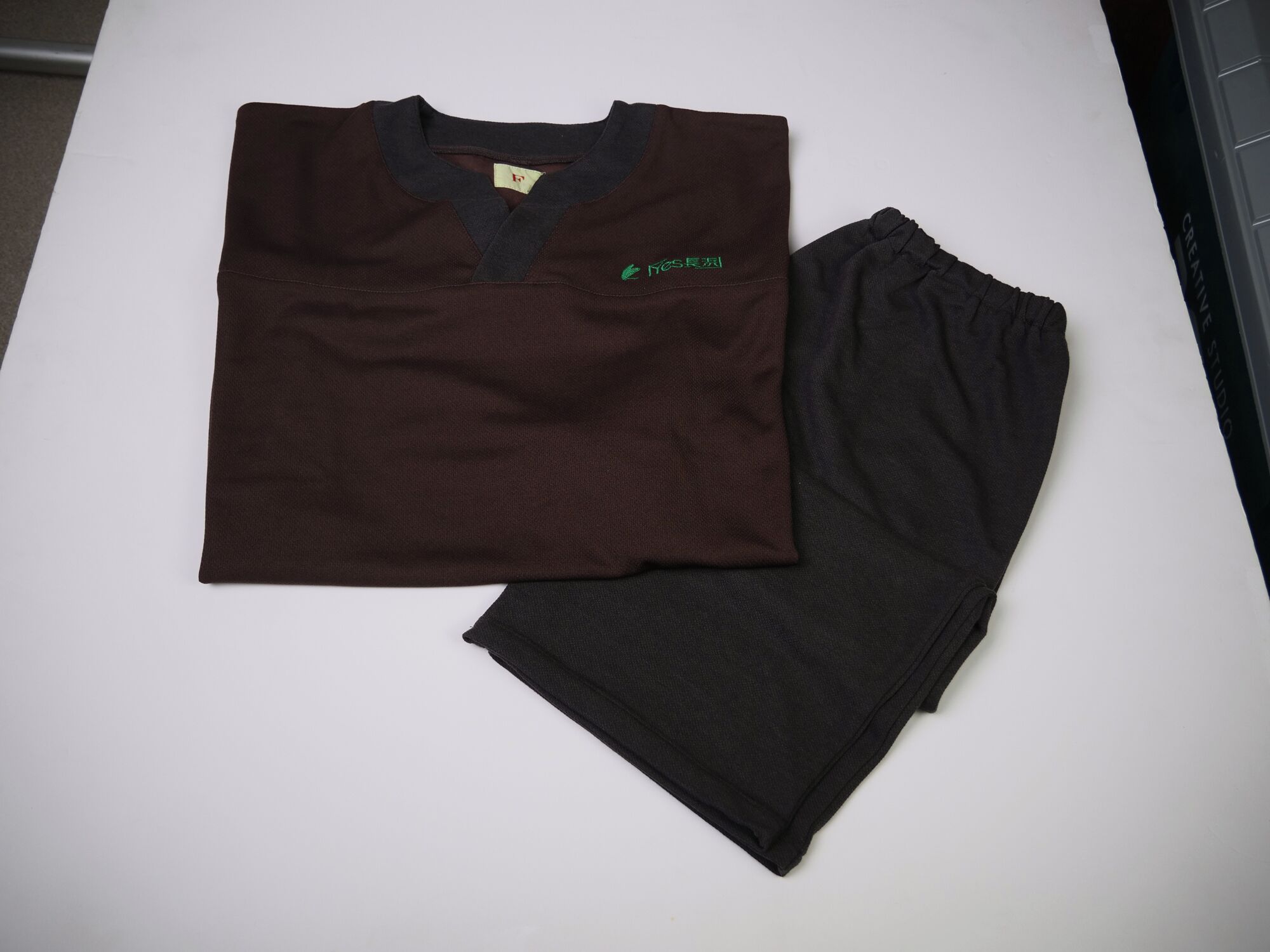 A folded dark brown shirt with a green logo and a black shirt on a white surface.