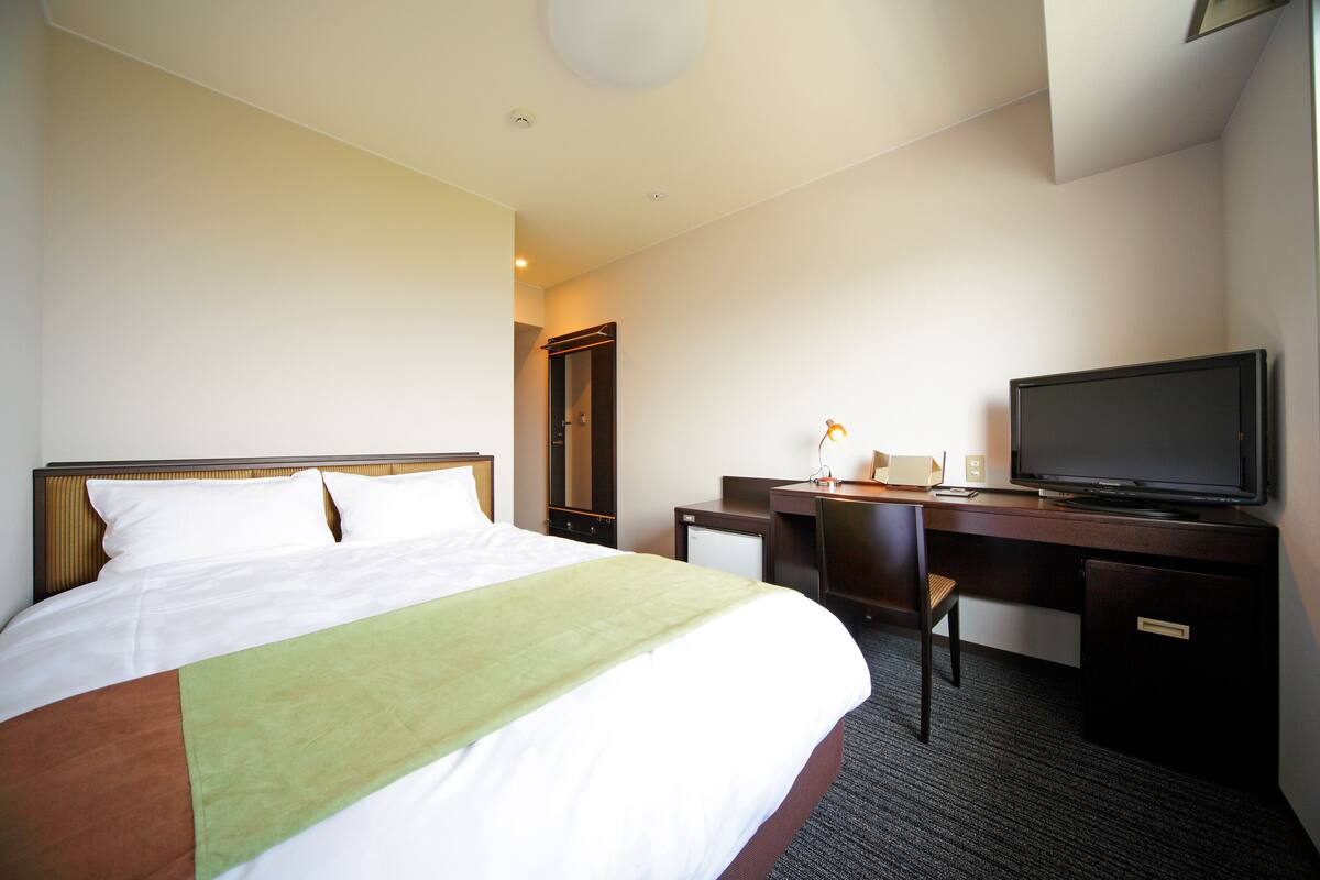 Une chambre d’hôtel équipée d’un lit, d’un bureau, d’une télévision et d’un petit réfrigérateur.