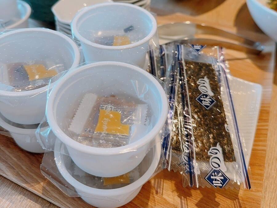 A table with several white cups containing tea, a bowl of food, and a packet of snacks.