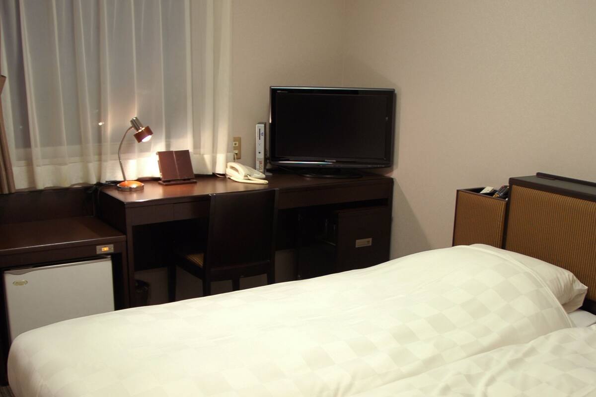 Une chambre d’hôtel équipée d’un lit, d’un bureau avec un ordinateur, d’une télévision et d’un appareil de climatisation.