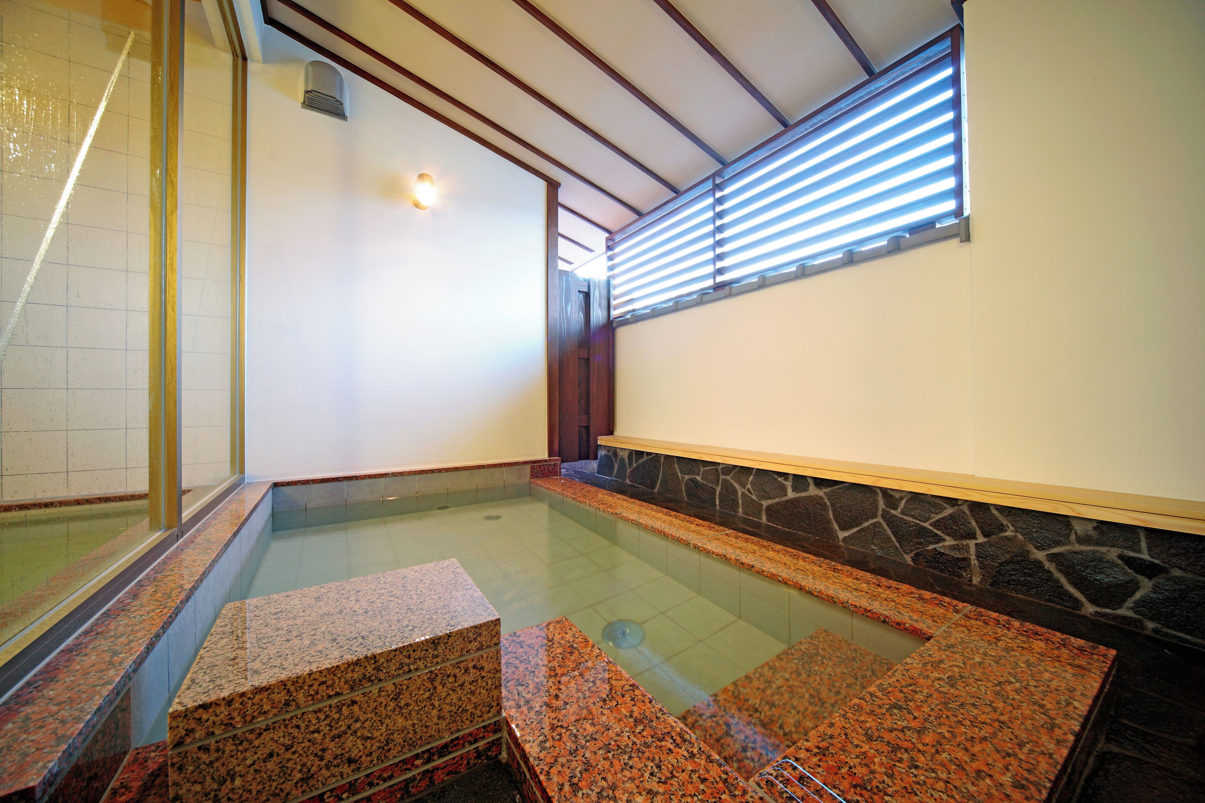 Un área de spa con un jacuzzi de paredes de vidrio, escalones de granito y una pared de piedra.