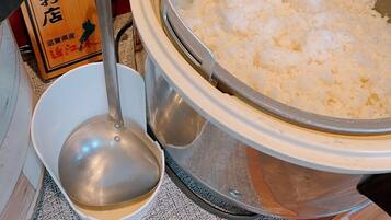 Een keuken met een rijstkoker vol witte rijst, een opscheplepel en een houten bordje met Japanse tekst.