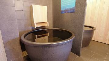 A stone-floored bathroom with a large stone bathtub, a wooden shelf, and a sign with Japanese text.