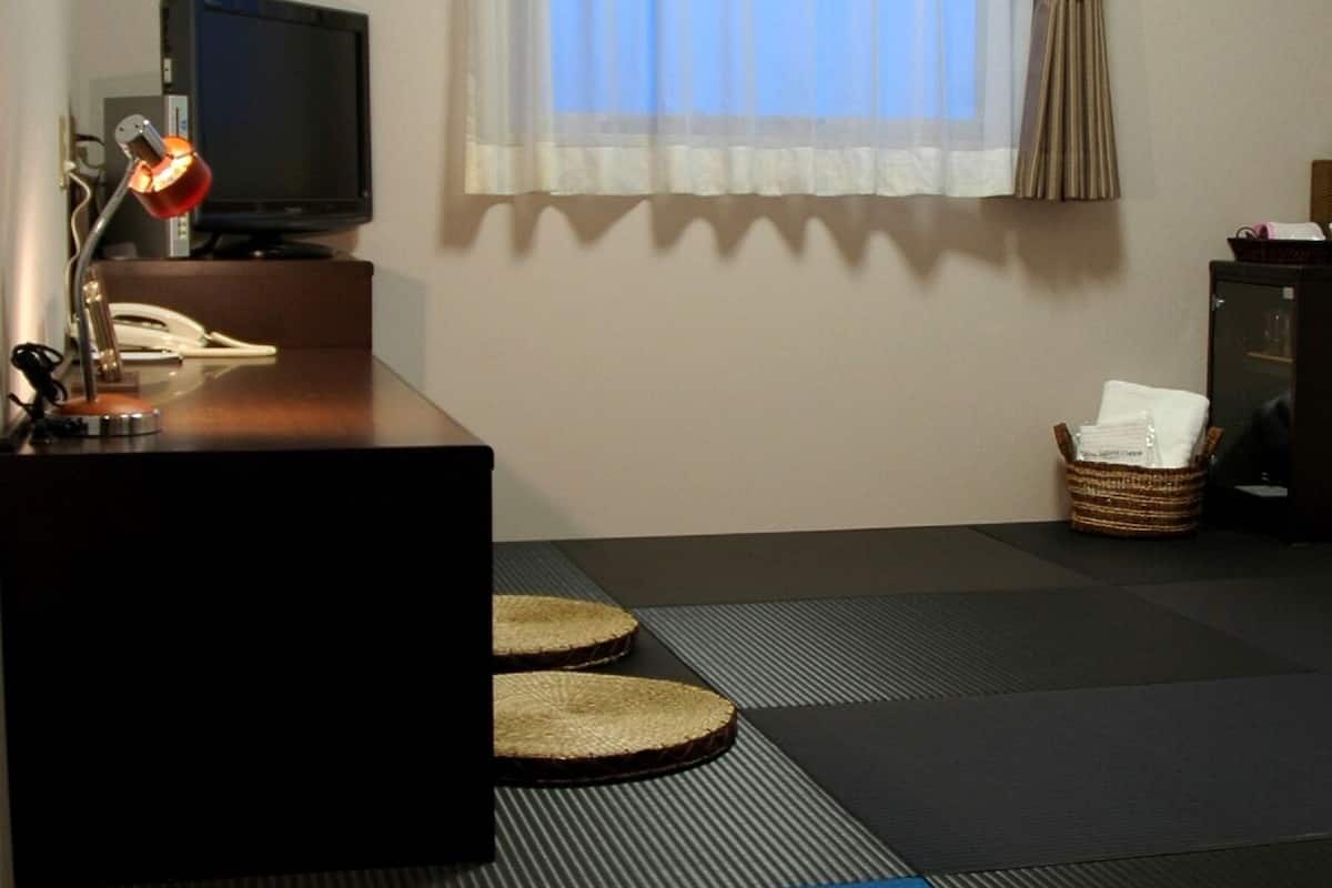 Une chambre avec un bureau, une télévision, une fenêtre avec des rideaux et un futon servant de lit.