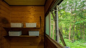 Eine Holzhütte mit drei weißen Körben auf Regalen und einem Fenster mit Blick auf einen Wald.