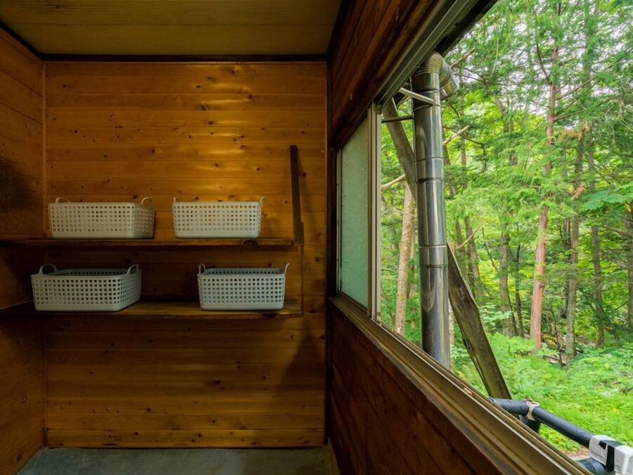 A wooden cabin with three white baskets on shelves and a window overlooking a forest.
