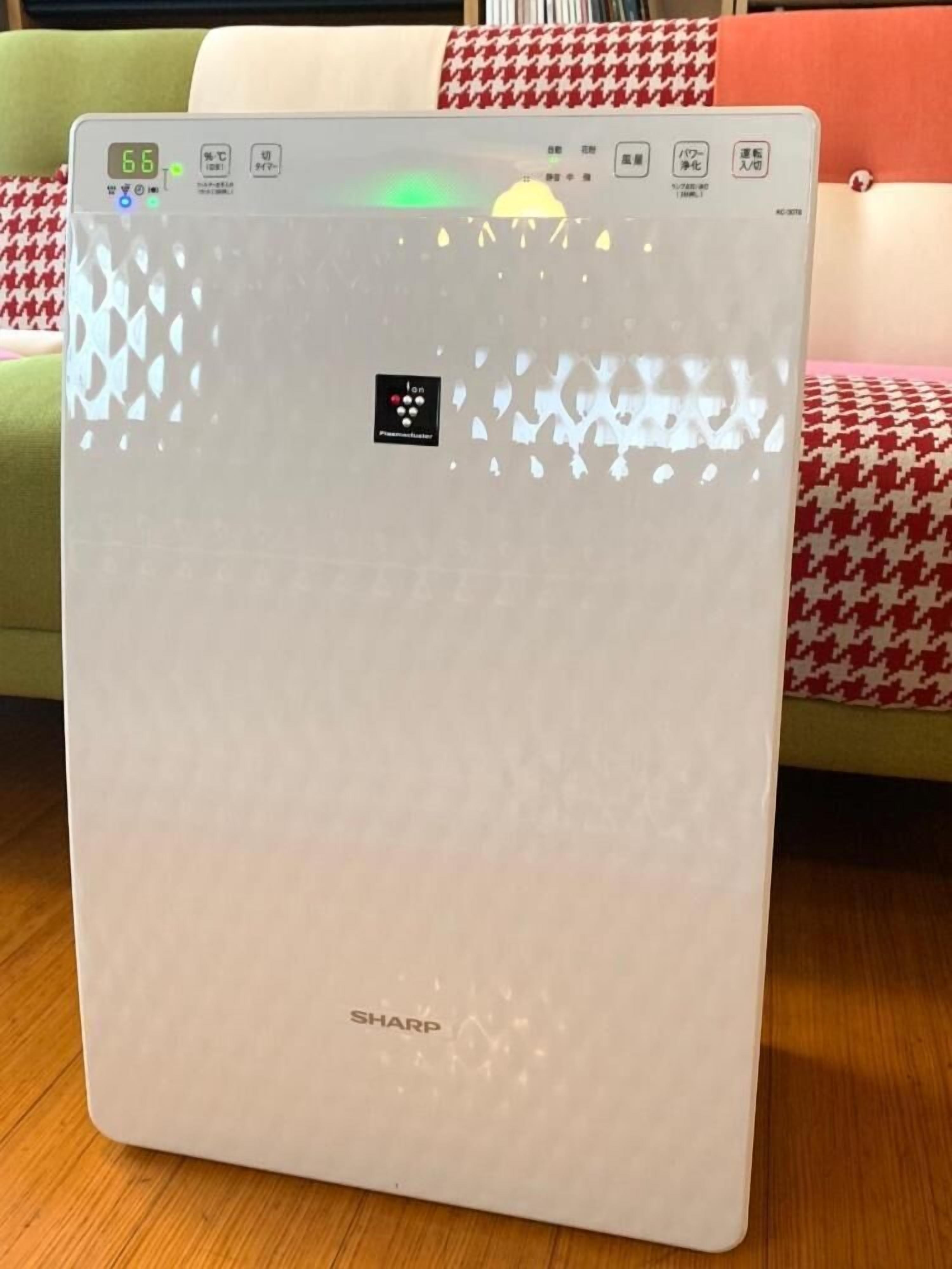 A white air purifier with a digital display and control panel, placed on a wooden floor.