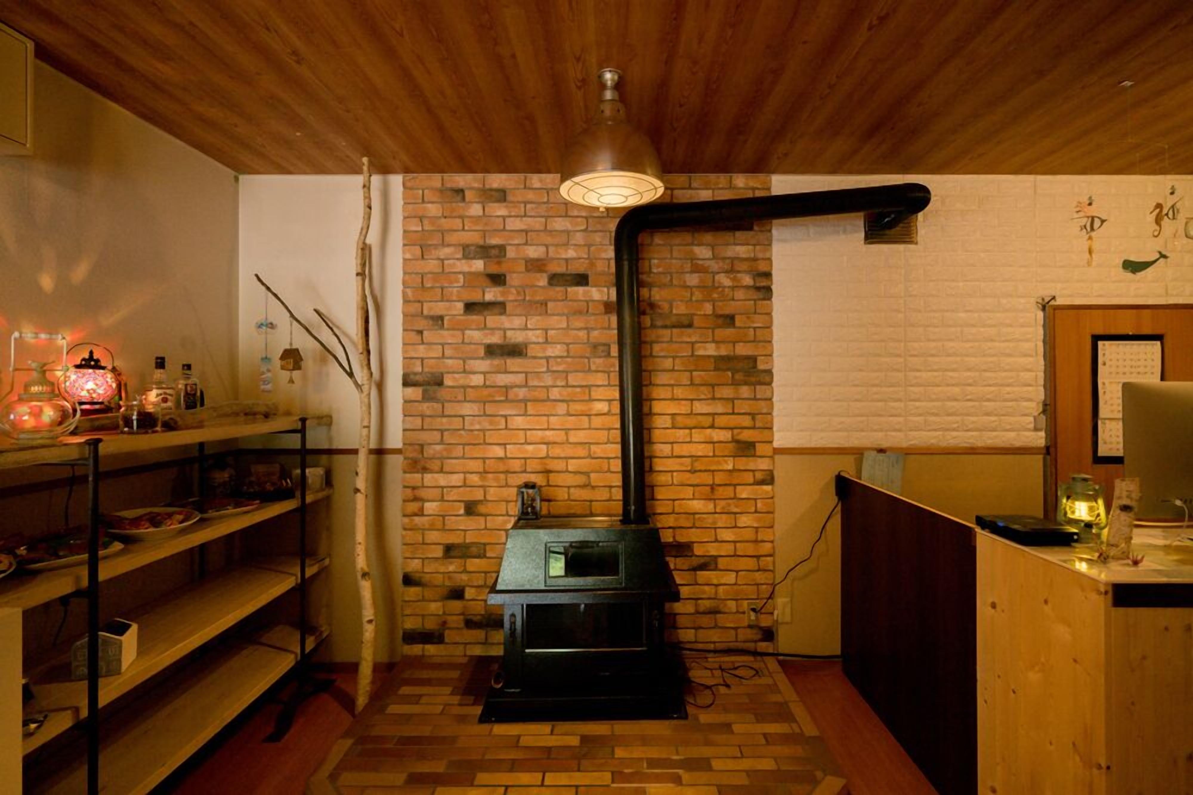 Een knus ingerichte kamer met een bakstenen muur, een houten plafond, een zwart fornuis en planken met diverse spullen.