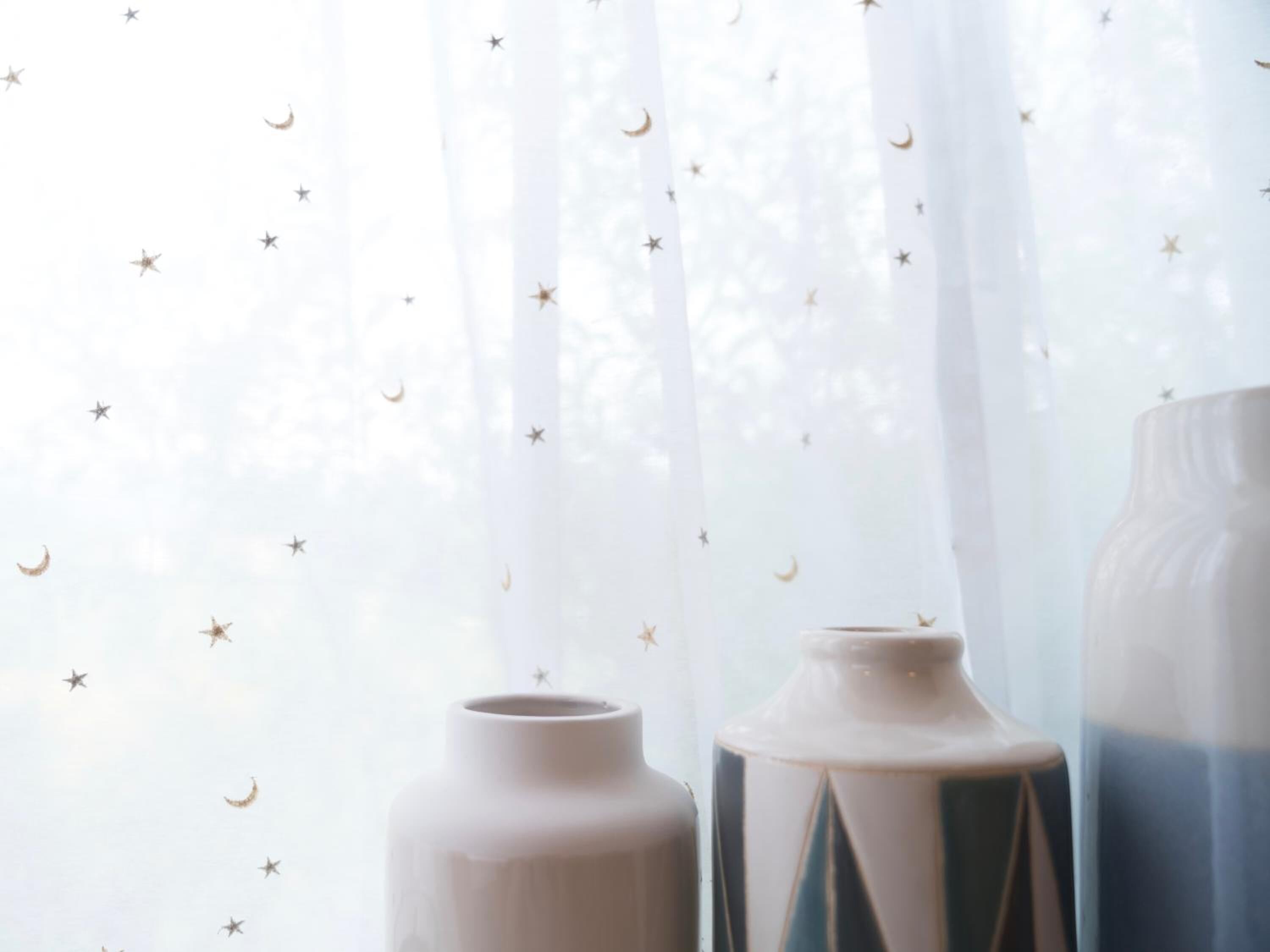 Una stanza con tende leggere che presentano un motivo a stella e crescente, e due vasi su un tavolo.