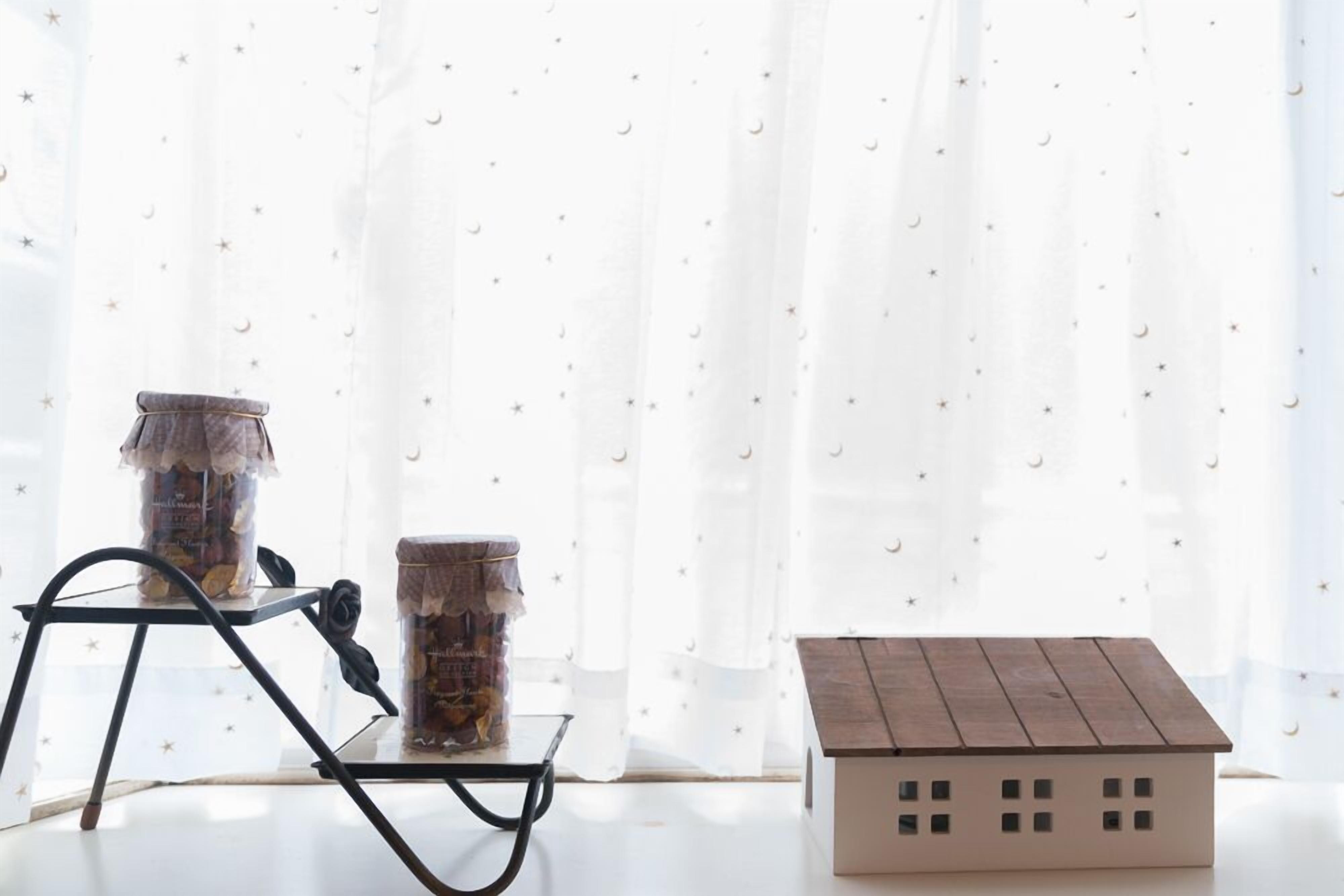 A room with a window, a small table with two jars, and a model house.