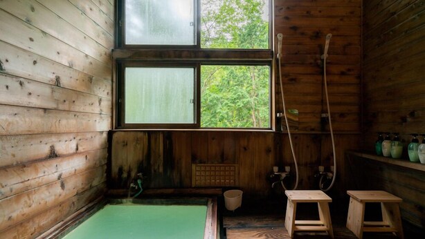Eine Holzhütte mit Whirlpool, Holzschemeln und einem Fenster mit Blick auf Grünfläche.