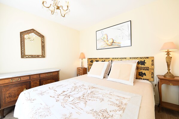 Ett hotellrum med en säng, en byrå, en spegel, en kristallkrona, en tavla och en lampa.
