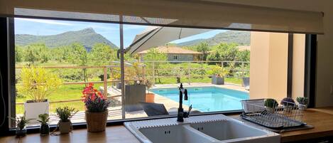 A kitchen with a large window overlooking a pool and mountains.