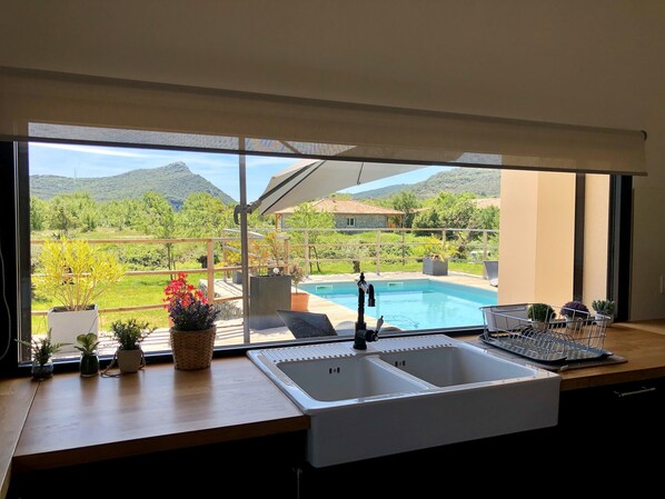 Una cocina con un amplio ventanal que da a una piscina y montañas.