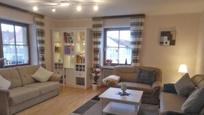 Una sala de estar con un sofá color beige, una mesa de centro blanca y una estantería.