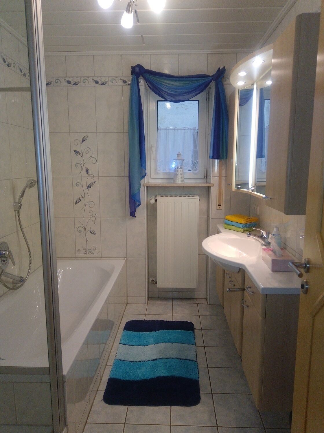 Un baño con bañera, ducha, lavamanos y ventana con cortinas.