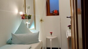 Un dormitorio pequeño y ordenado con cama, mesita de noche, espejo y ventana con vistas.