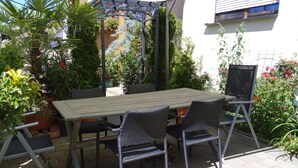 Un patio con una mesa y sillas, rodeado de plantas en macetas y un arco metálico decorativo.