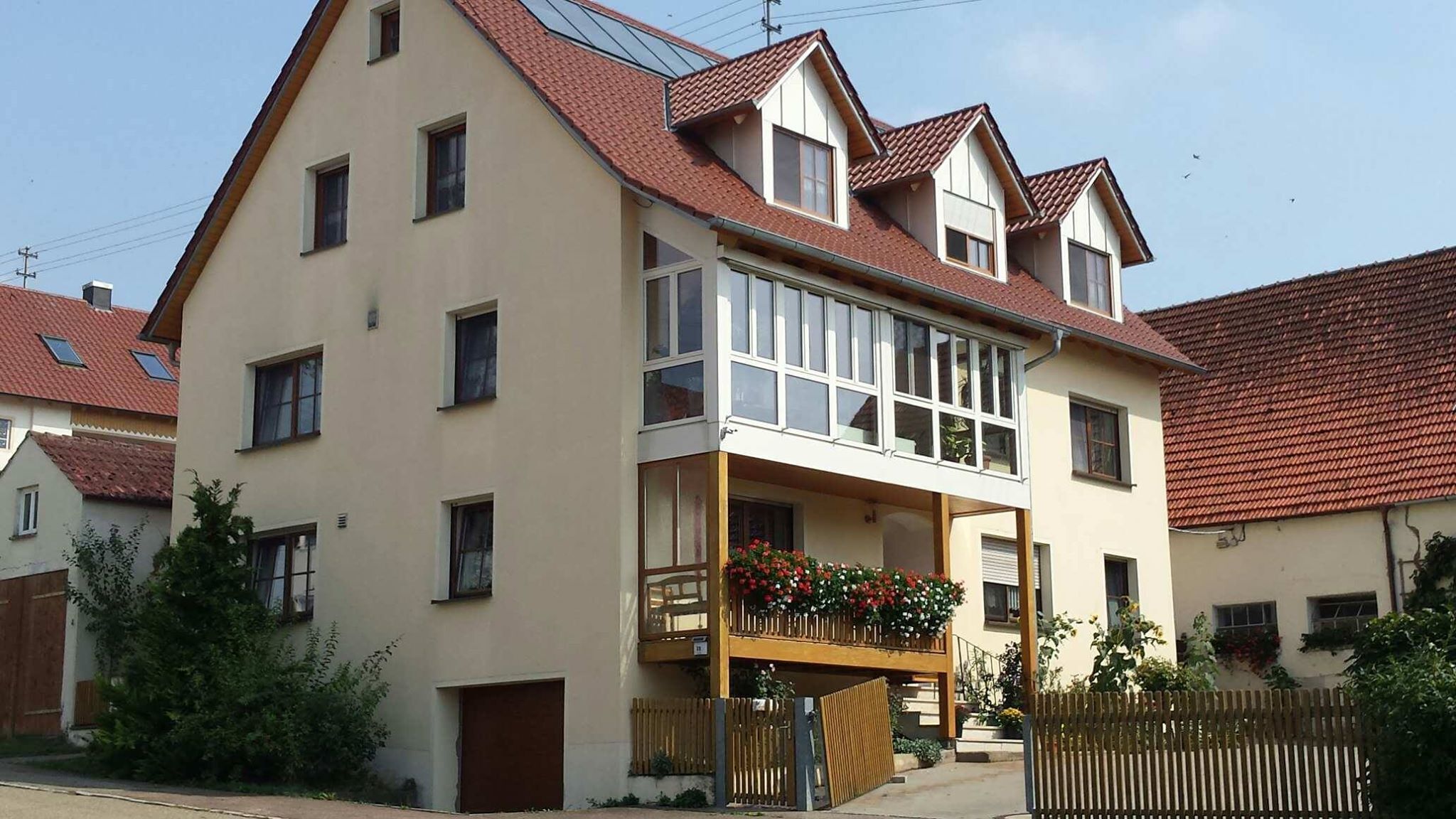 Una casa de dos pisos con balcón, garaje y cerca de madera.