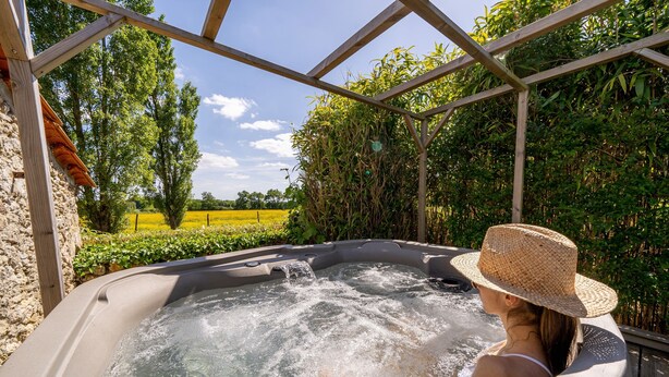 A hot tub with a wooden pergola structure, surrounded by lush greenery and a clear sky. - Comfortable cottage in peace between sea and marsh! (Sallertaine)