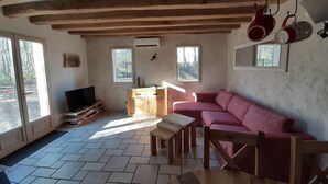 A cozy living room with a wooden ceiling, a red sofa, a wooden table, and a TV on a wooden stand. - La Haute Bédinière, B&B near Chambord (Crouy-Sur-Cosson)