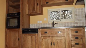 A kitchen with wooden cabinets, a dishwasher, an oven, and a window with a view of trees. - La Haute Bédinière, B&B near Chambord (Crouy-Sur-Cosson)
