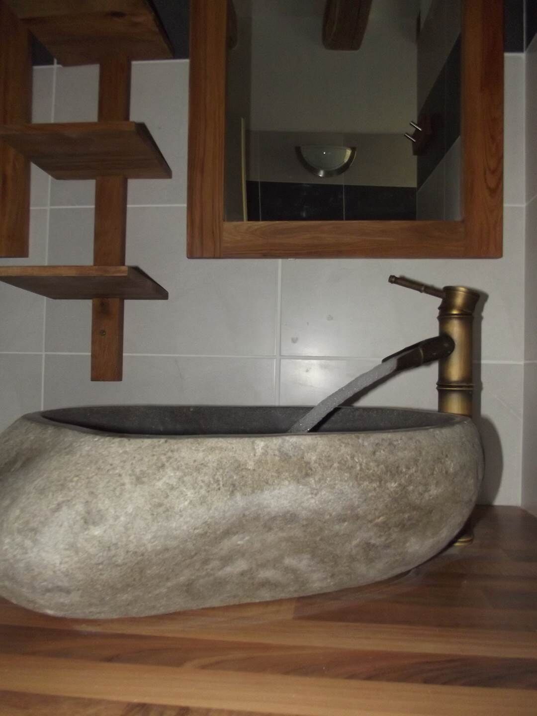 A stone sink with a brass faucet mounted on a wooden countertop.