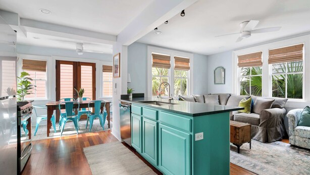 A spacious kitchen with teal cabinetry, a dining area with blue chairs, and a living room with a sofa and a coffee table. - Charleston Riviera | King Street Home - Walkable! (Charleston)