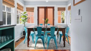 A dining area with a wooden table and turquoise chairs, surrounded by windows with blinds. - Charleston Riviera | King Street Home - Walkable! (Charleston)