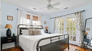 A bedroom with a bed, nightstands, a ceiling fan, and a view through a window with curtains. - Charleston Riviera | King Street Home - Walkable! (Charleston)