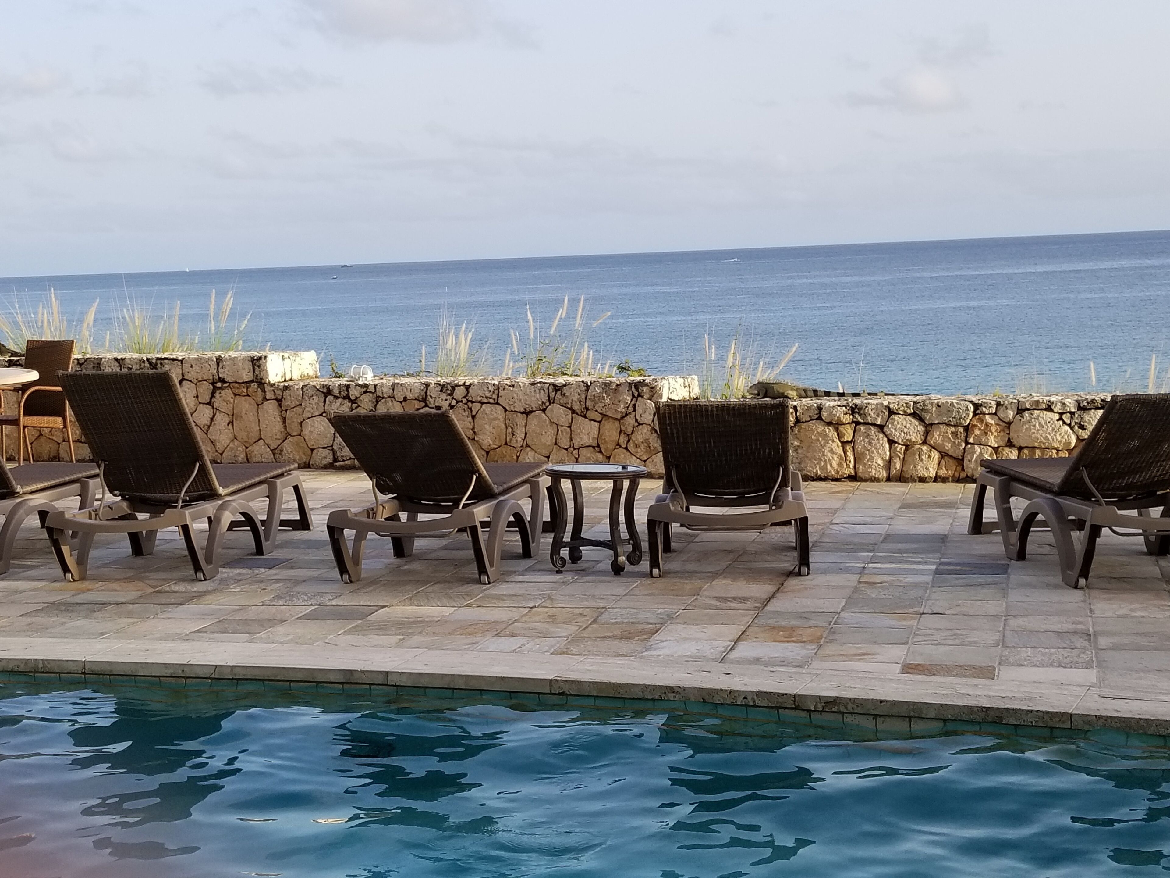 A poolside area with lounge chairs and a stone wall overlooking the sea.