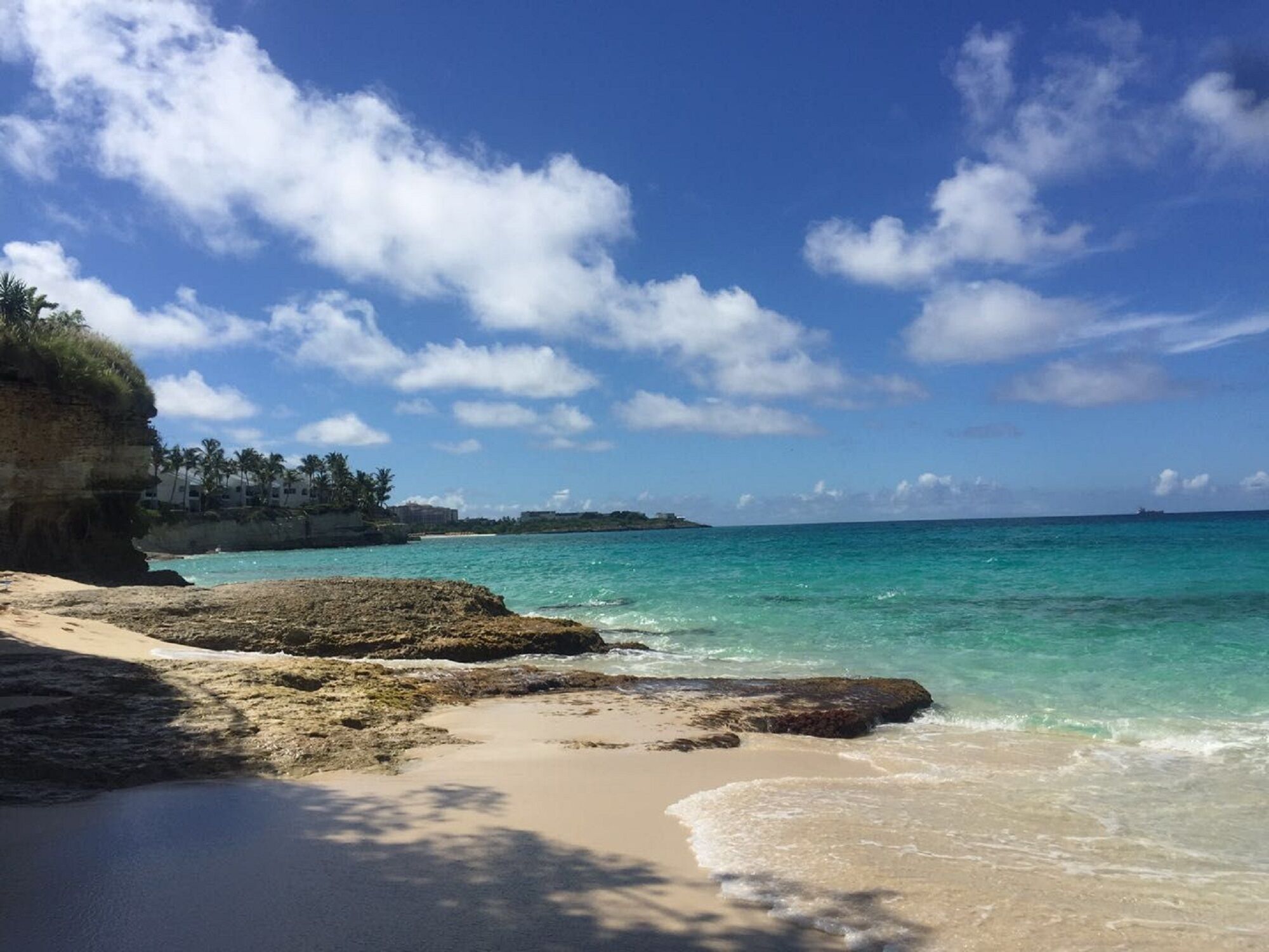Une plage à l’eau turquoise et limpide, avec un rivage sablonneux et des affleurements rocheux.
