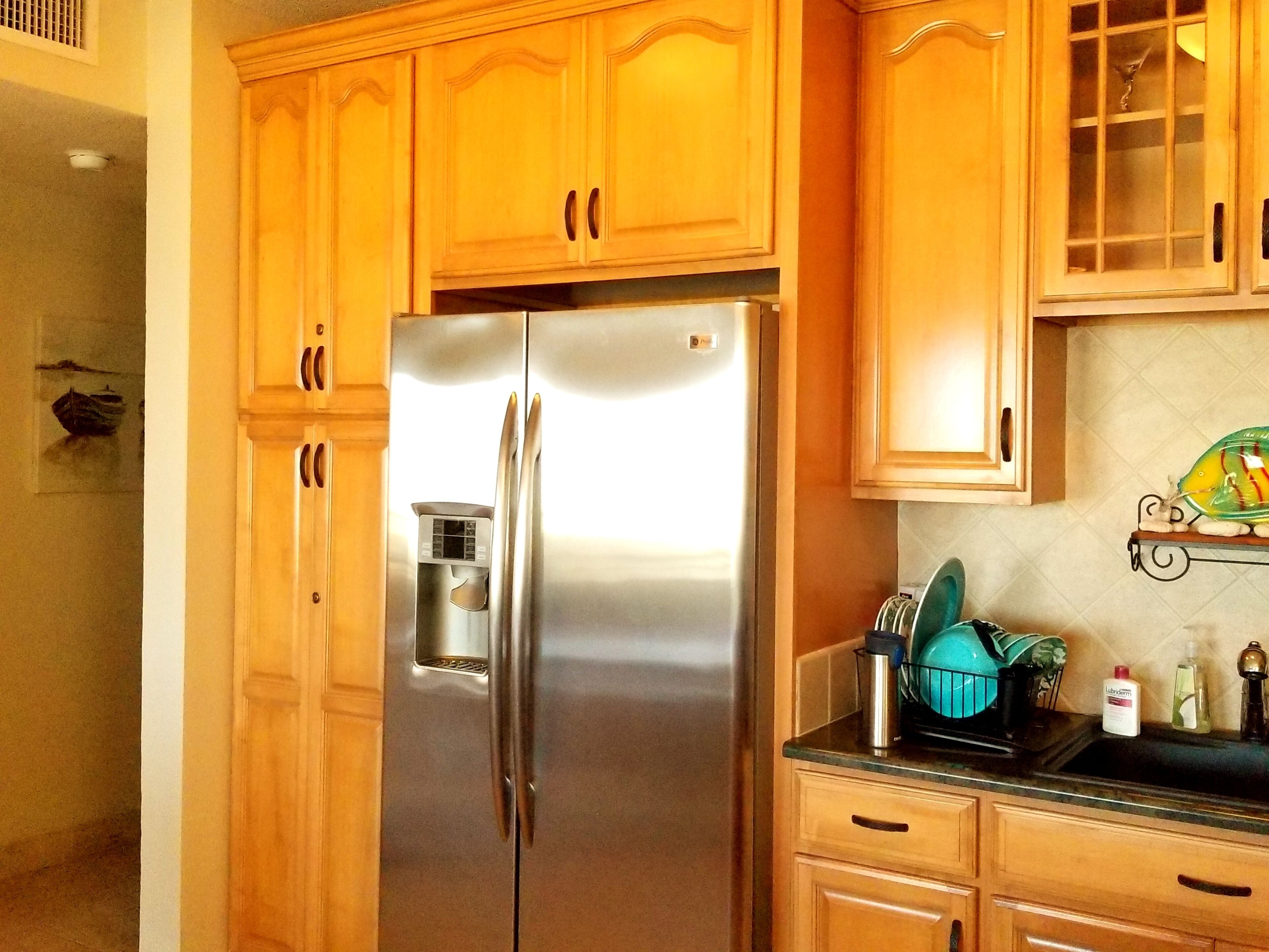 Una cocina con armarios de madera, un refrigerador de acero inoxidable y una encimera con vajilla y productos de limpieza.