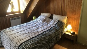 Ein Schlafzimmer mit schrägem Dach, einem Bett mit gemusterten Bettbezügen, einer Nachttischlampe und einem an der Wand hängenden Bild.