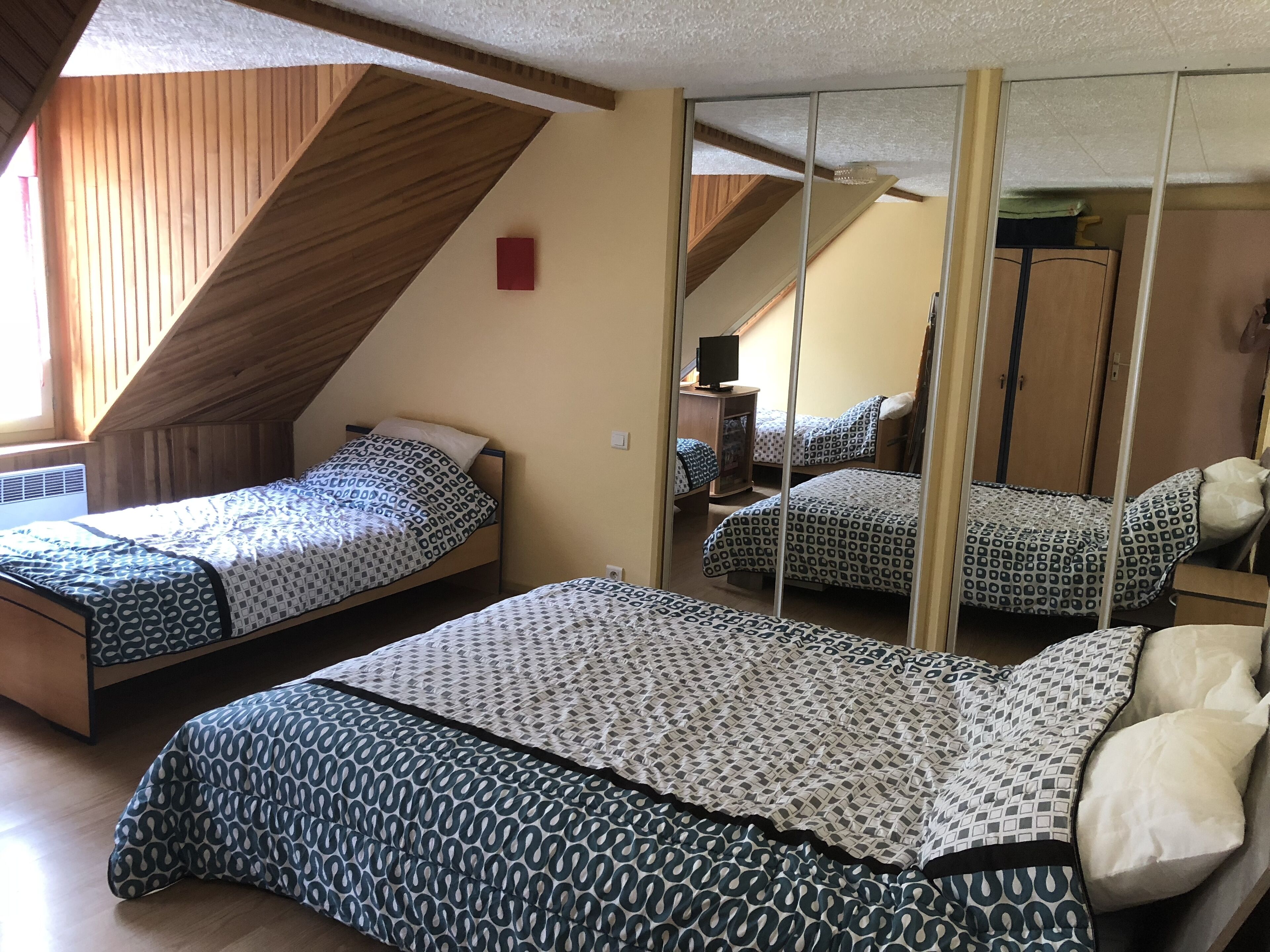 A bedroom with two single beds, a wooden sloped ceiling, and a large mirror reflecting the room.