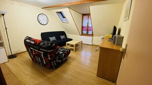 Ein gemütlicher Wohnbereich mit Sofa, kleinem Tisch, einer Uhr und einem Schreibtisch mit Stuhl.