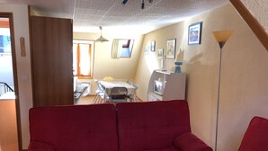 Ein Wohnzimmer mit rotem Sofa, einem Essbereich mit Tisch und Stühlen, einem Fernseher und einer Lampe.