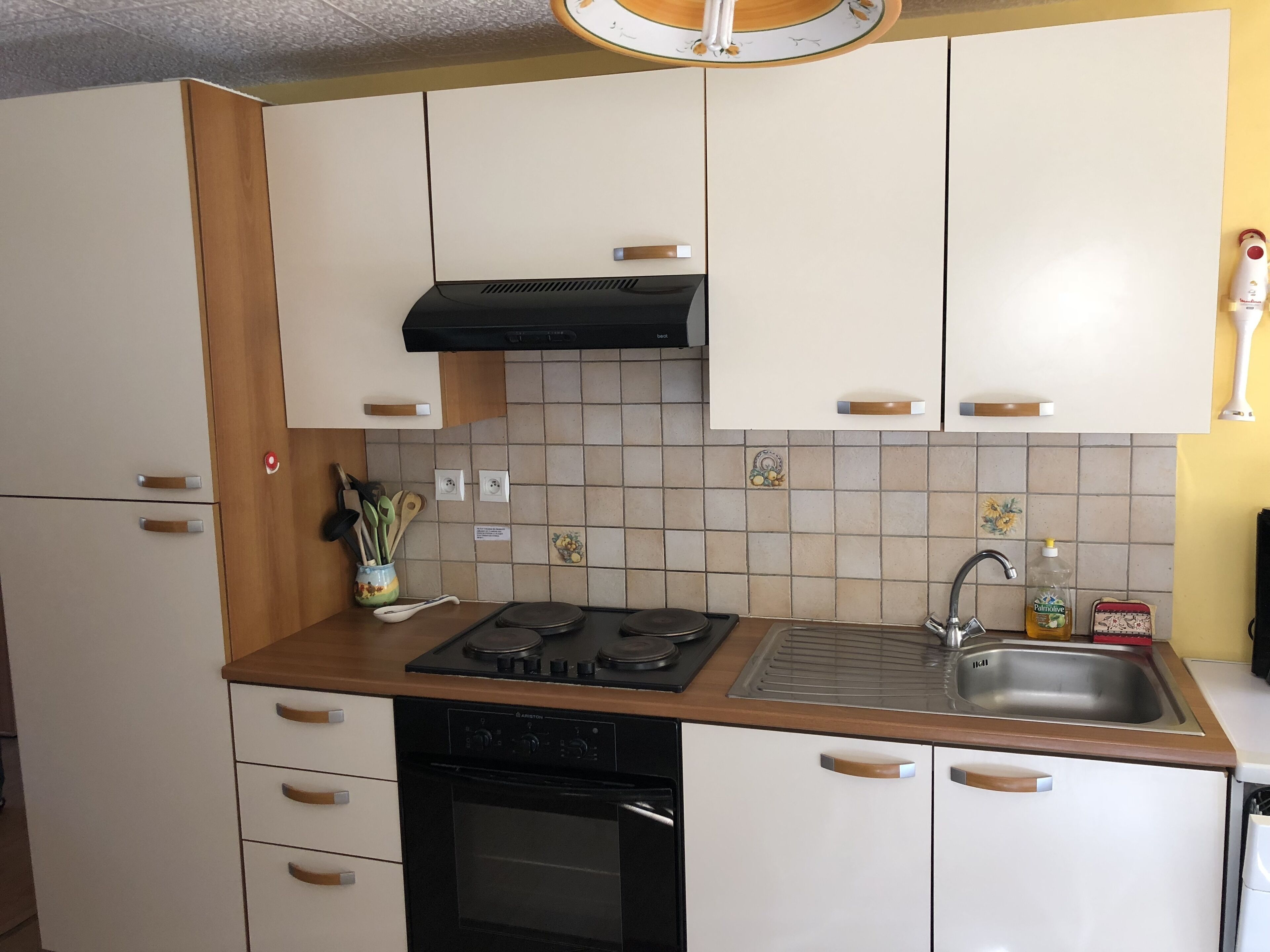 Una cocina con armarios blancos, estufa negra, un lavamanos y un salpicadero de azulejos.